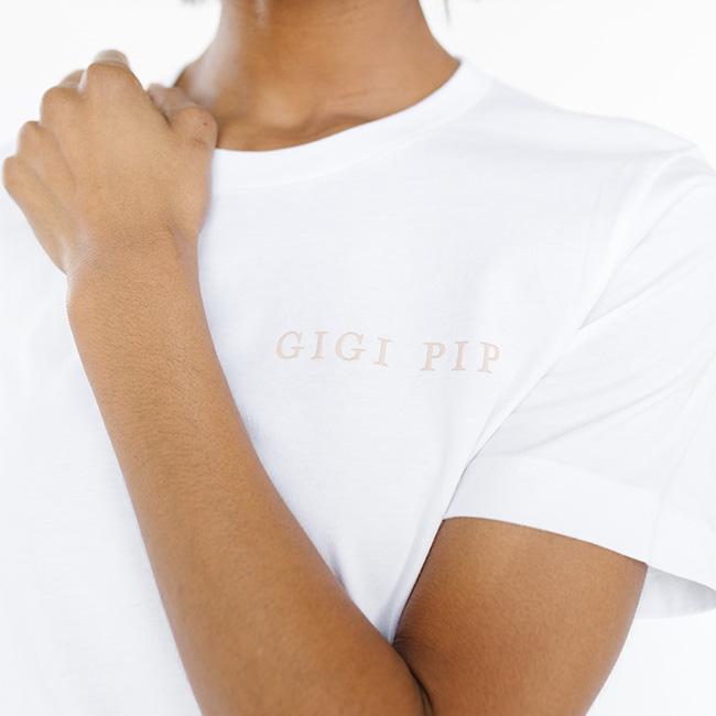 Person wearing a white t-shirt with 'GIGI PIP' text against a white background #color_white