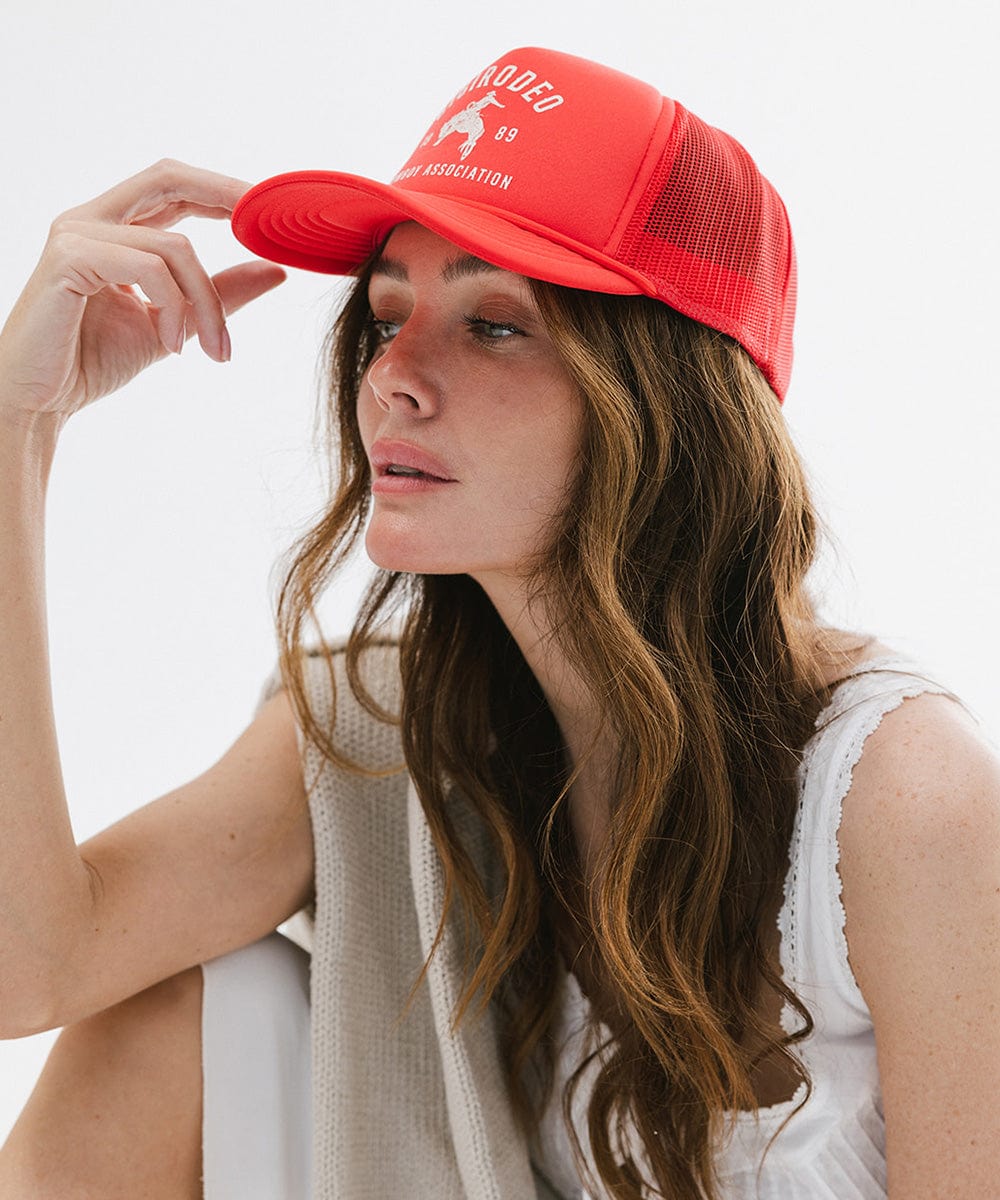 Woman wearing a vintage red cap with golden 'GIGIRODEO' text and logo, and a white top against a plain background #color_vintage red