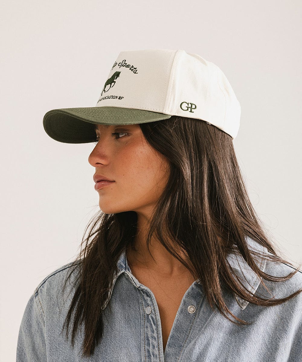 Woman wearing a white and green cap with branding on a plain background #color_cream - dark green