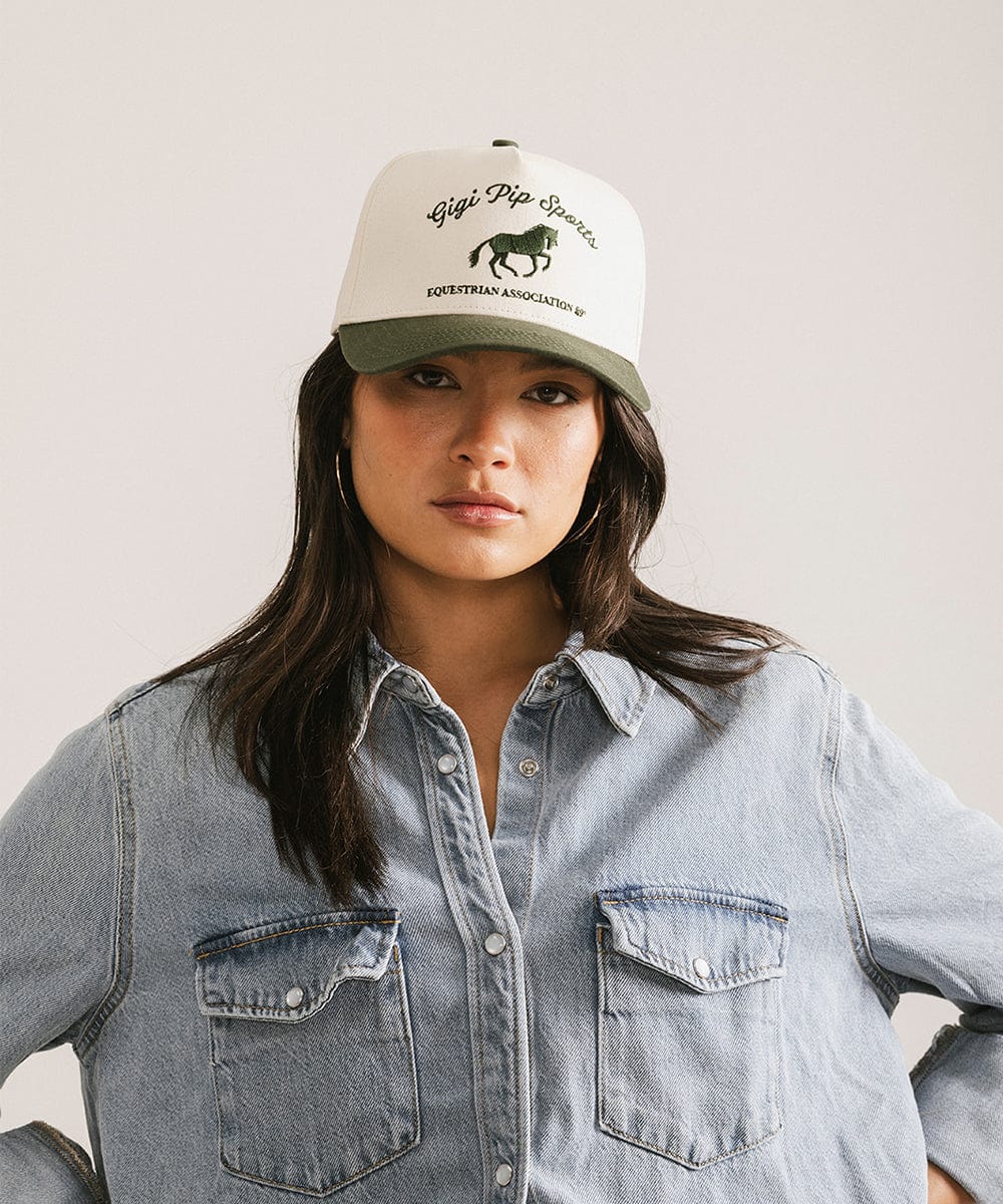 Person wearing a cap with a logo and text, standing against a plain background #color_cream - dark green
