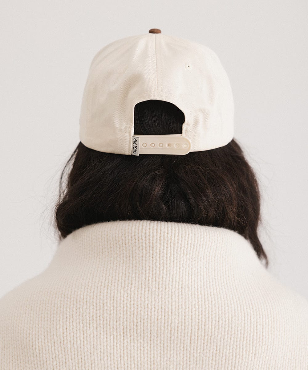Woman wearing a cream and chocolate brown Trucker hat and a white sweater against a plain background #color_cream - chocolate brown