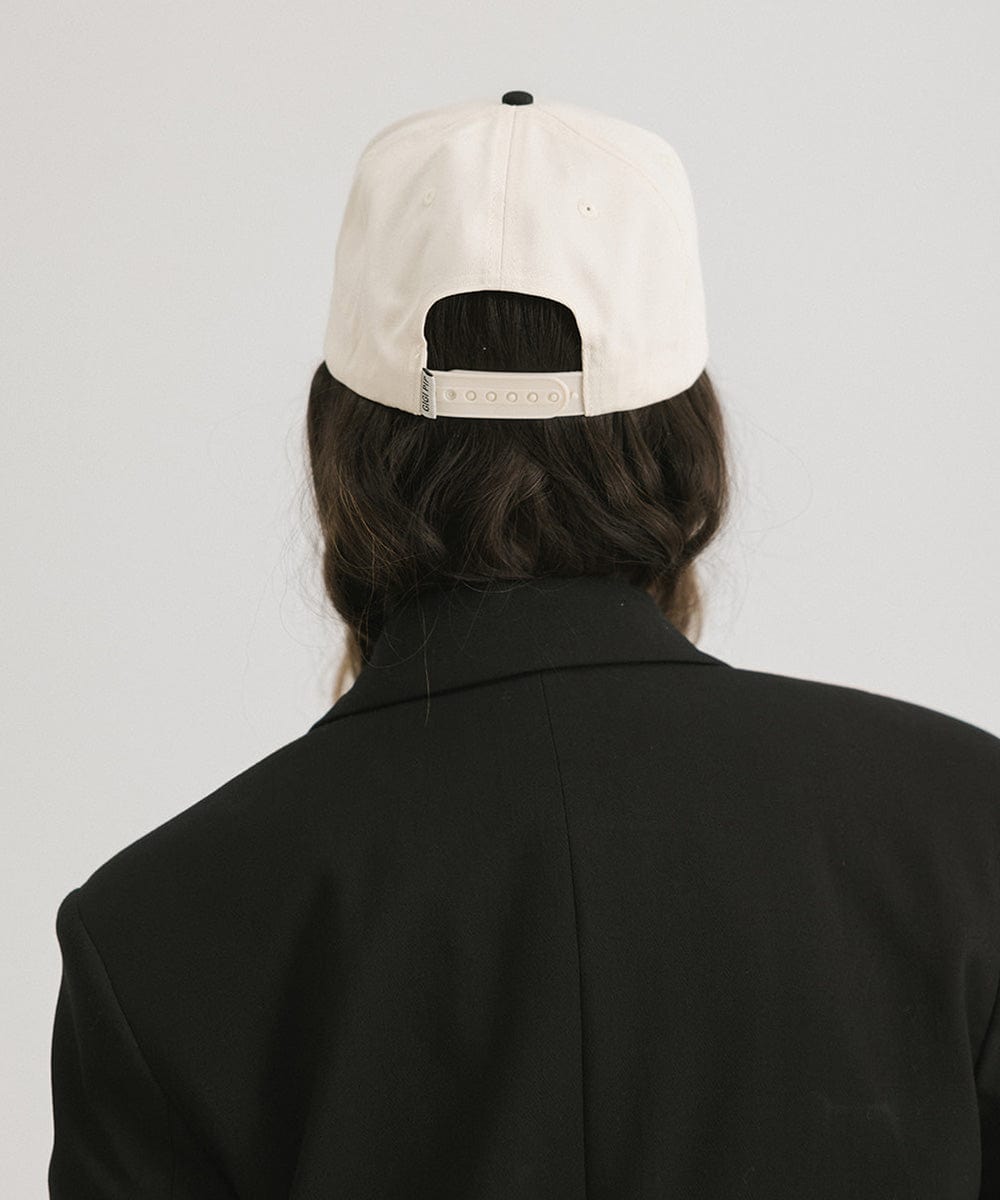 Woman wearing a cream and black Trucker hat and a black blazer against a plain background #color_cream - black