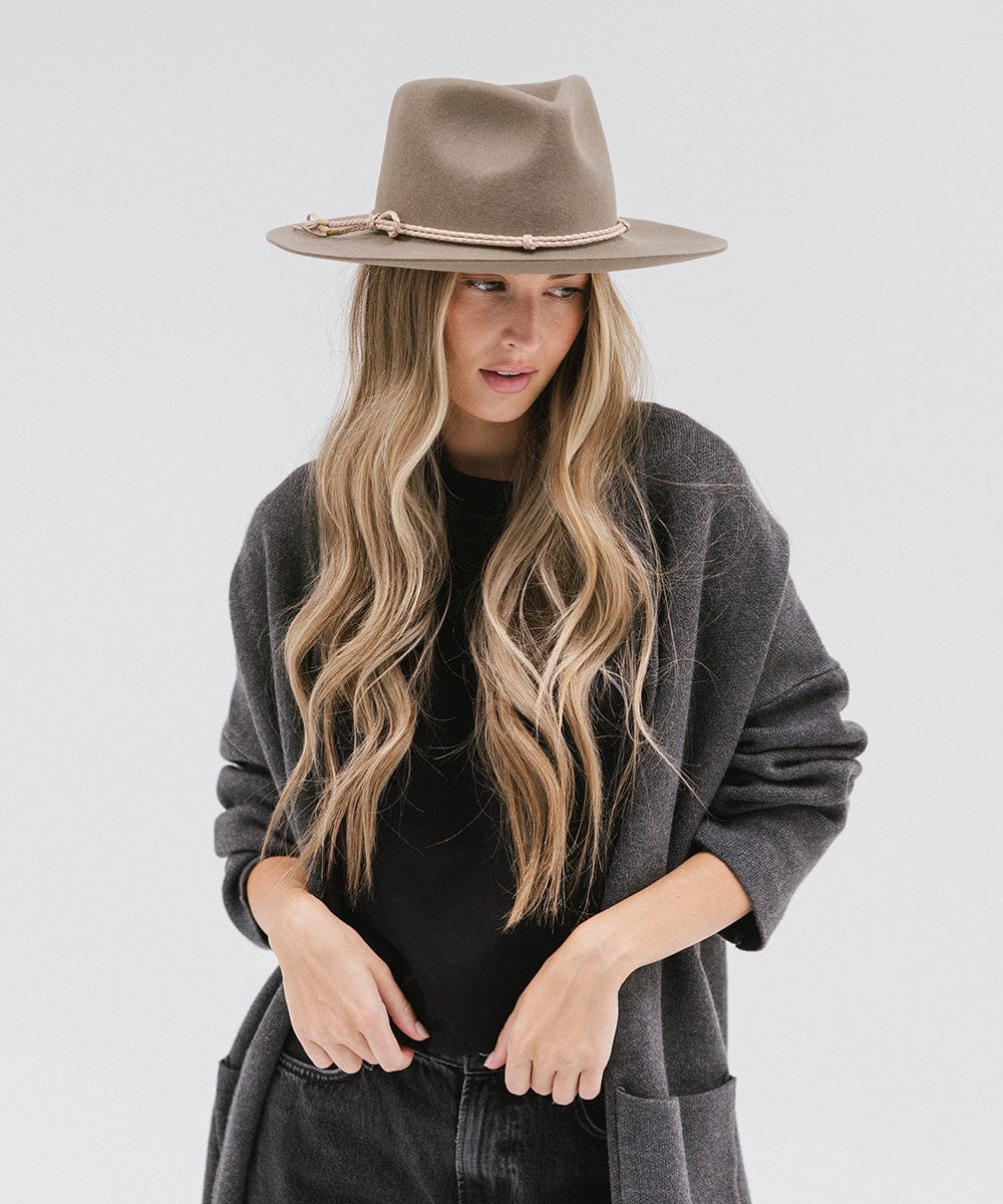 Woman wearing cowboy hat with a beige lasso braided hat band and a black t-shirt with grey jacket, posing against a plain background #color_beige
