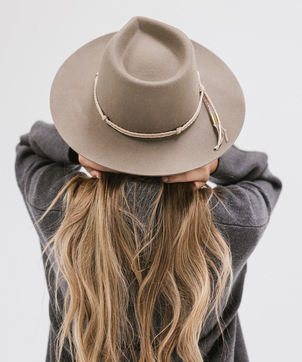 Person with long hair wearing cowboy hat with a beige lasso braided hat band and a grey sweater against a plain background #color_beige