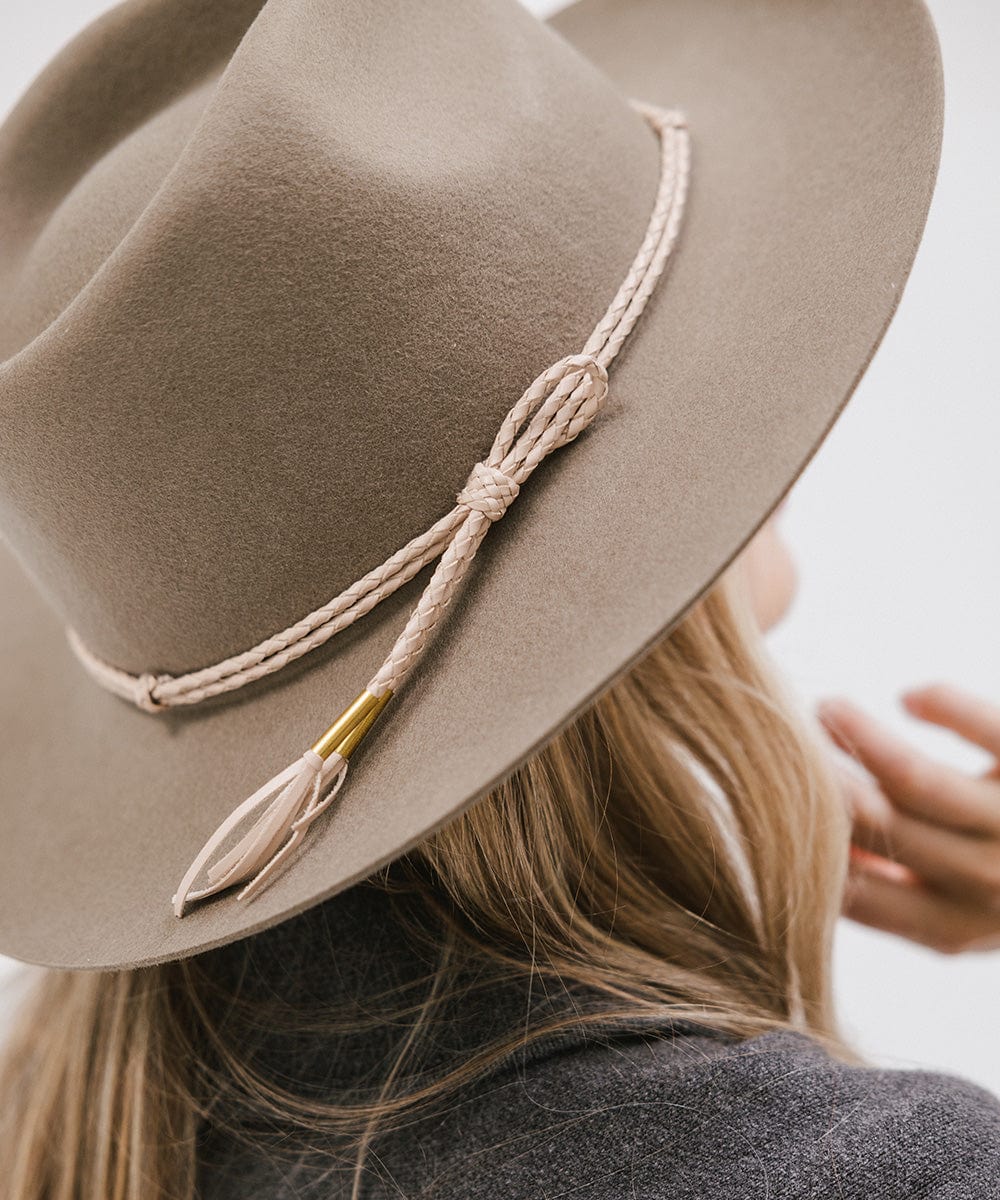 A cowboy hat with a beige lasso braided hat band being worn by someone against a plain background #color_beige