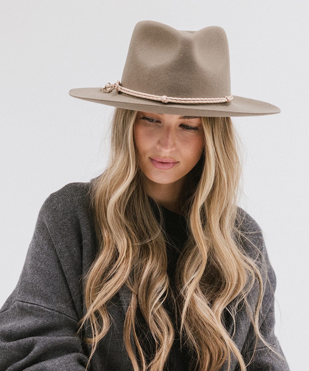 Woman wearing cowboy hat with a beige lasso braided hat band and a grey sweater against a plain background #color_beige
