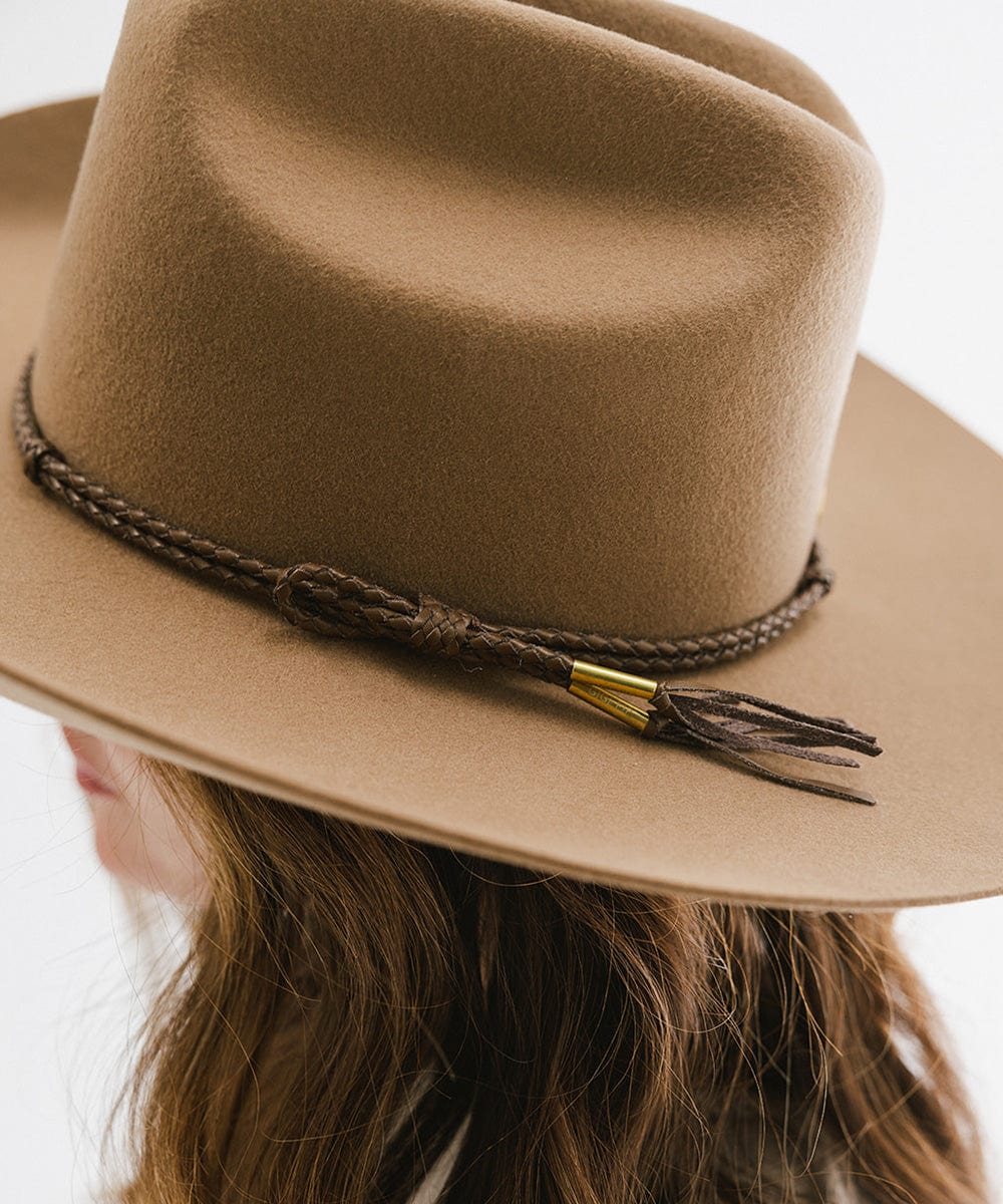 A tan cowboy hat with a brown lasso braided hat band, worn by someone against a plain background #color_brown