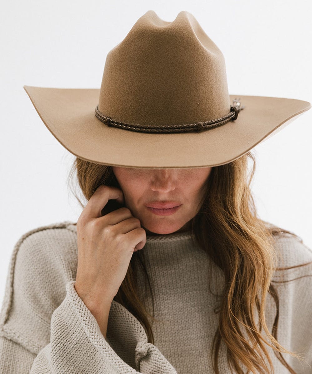 Woman wearing tan cowboy hat with a brown lasso braided hat band and a grey sweater, posing against a plain background #color_brown