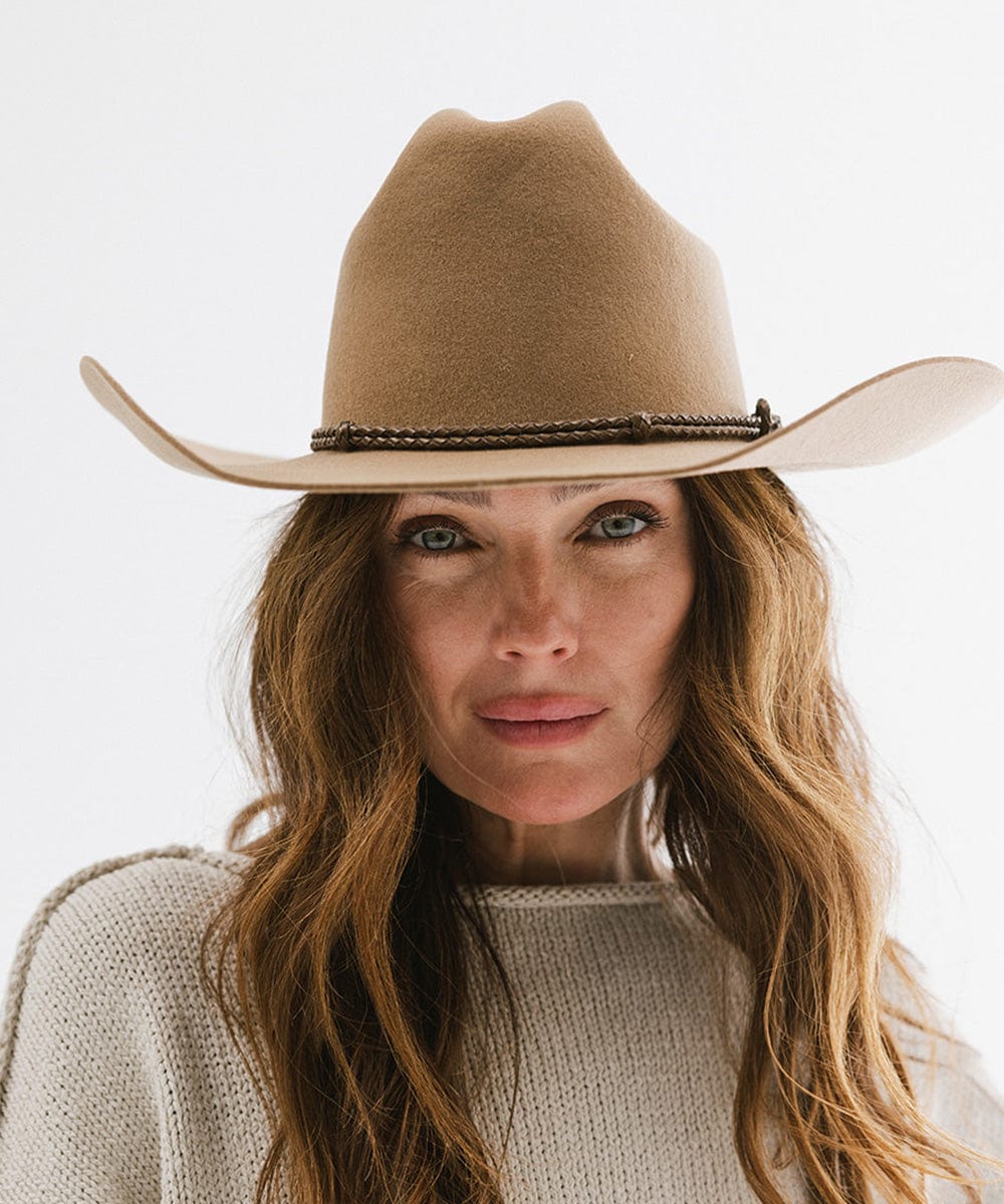 Woman wearing tan cowboy hat with a brown lasso braided hat band and a grey sweater against a plain background #color_brown