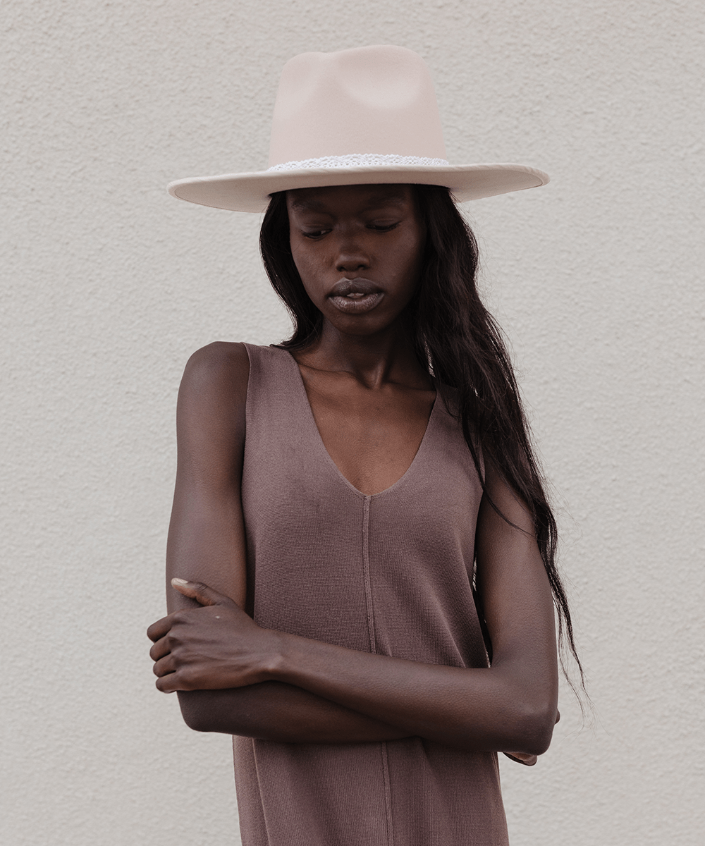 Woman wearing a cream hat with a white lace band and a brown top against a plain background #color_white