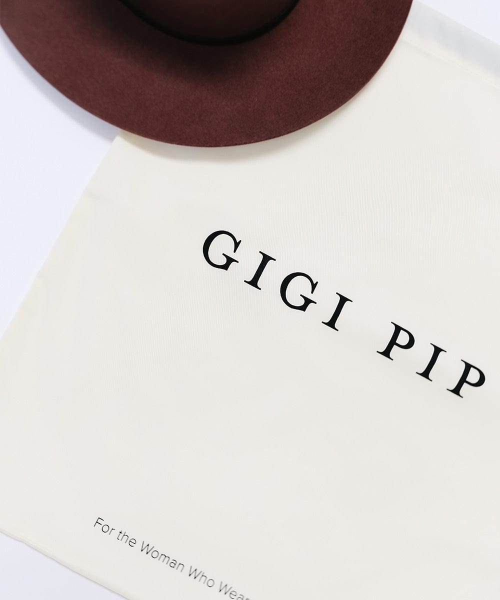 A maroon hat on a white hat keepsake bag with the GIGI PIP brand logo printed in black on the front against a plain background #color_white