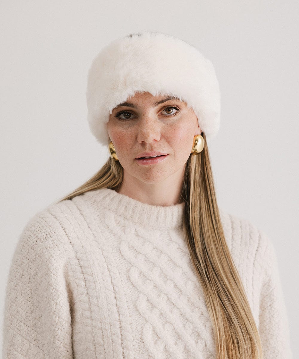 Woman wearing a winter white colored fur headband and a white sweater against a plain background #color_winter white