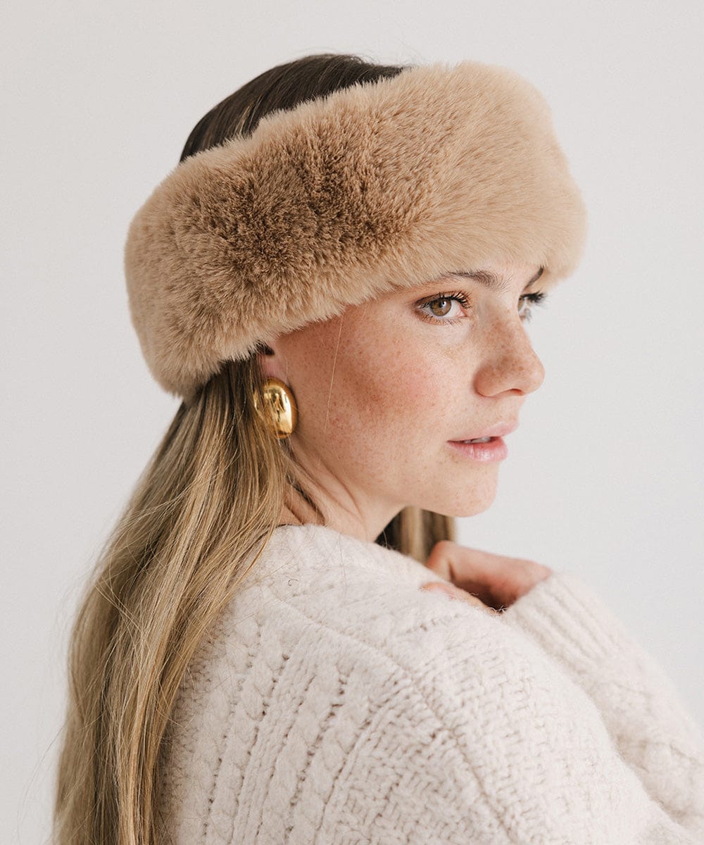 Woman wearing a tan fur headband and a white sweater, posing sideways against a plain background #color_tan