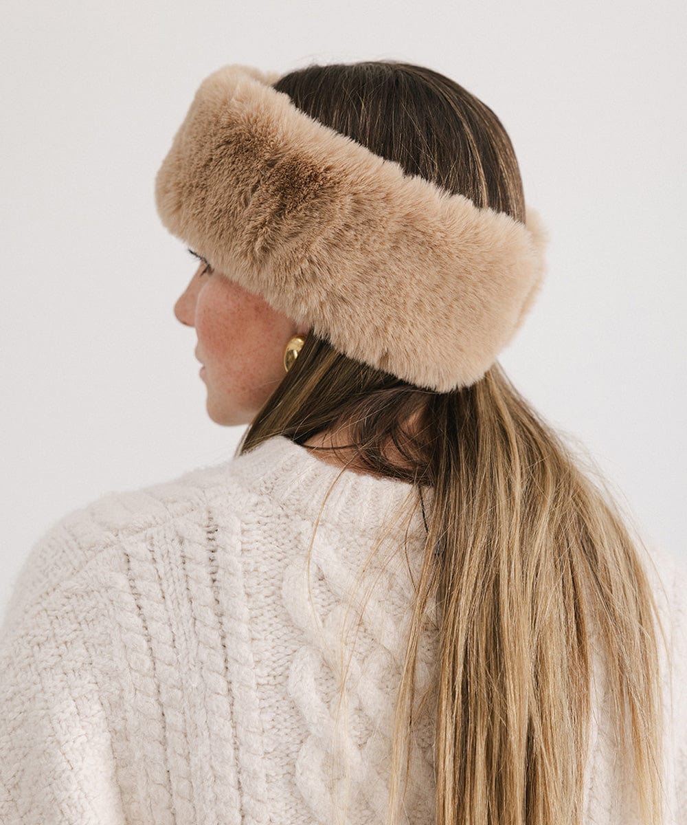 Woman wearing a tan fur headband and a white sweater, facing sideways against a plain background #color_tan