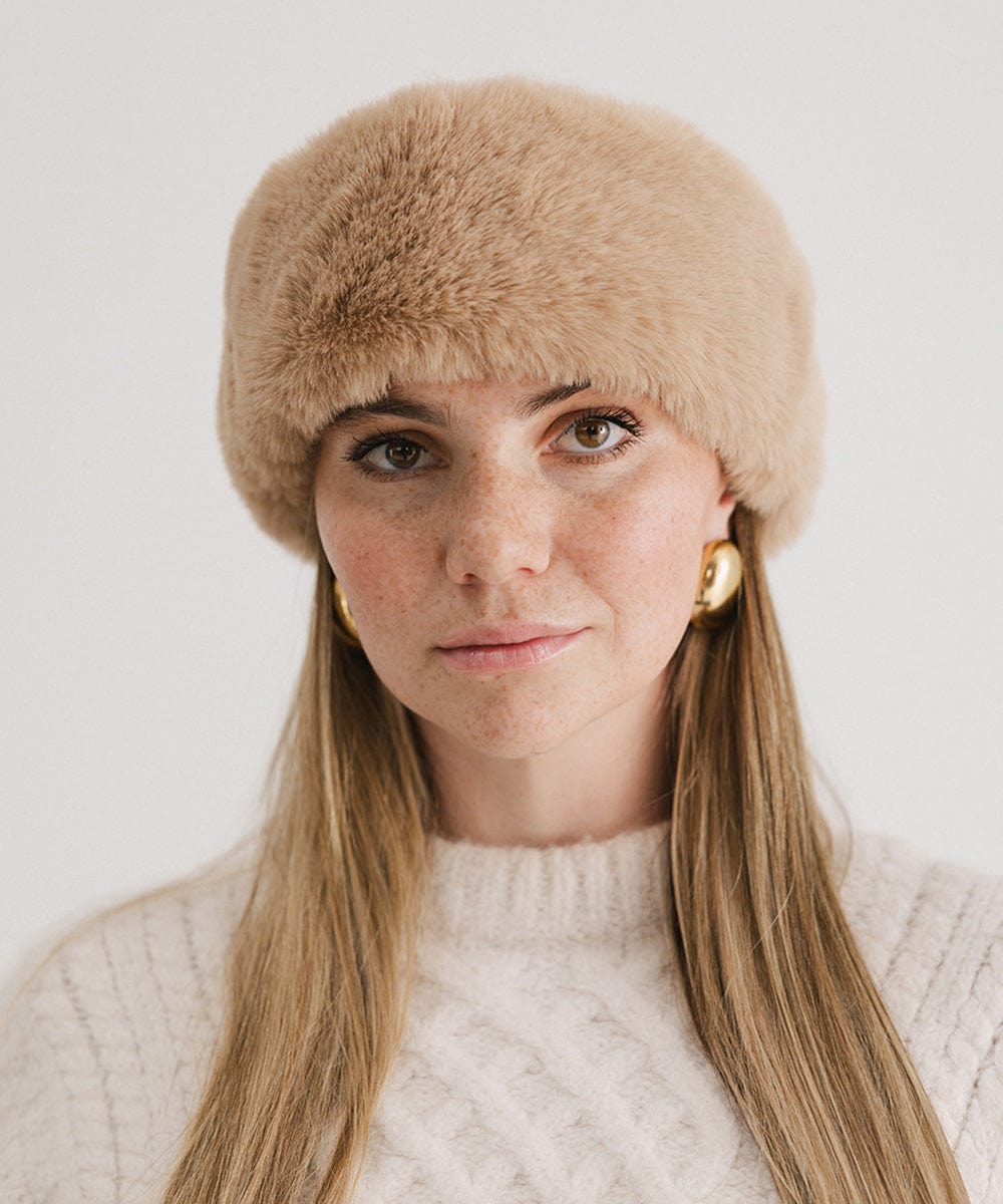 Woman wearing a tan fur headband and a white sweater against a plain background #color_tan