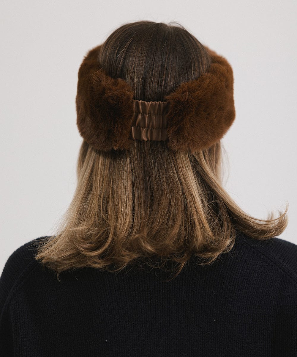 Woman wearing a brown fur headband and a black sweater, facing behind against a plain background #color_brown