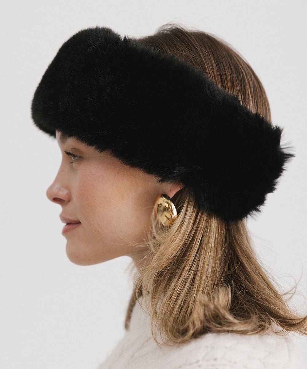 Woman wearing a black fur headband and a white sweater, facing sideways against a plain background #color_black