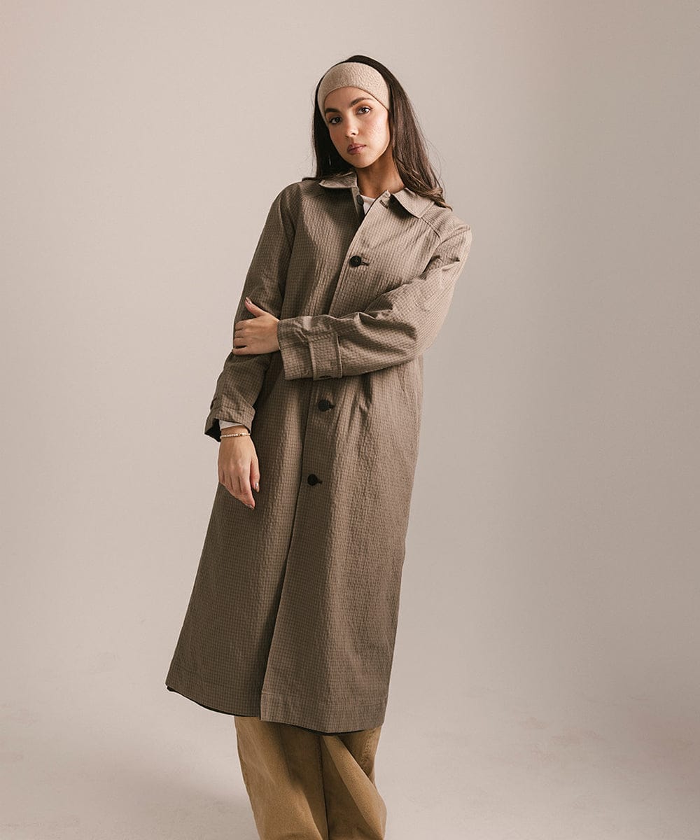 Woman wearing a long brown coat and tan headband against a plain background #color_tan