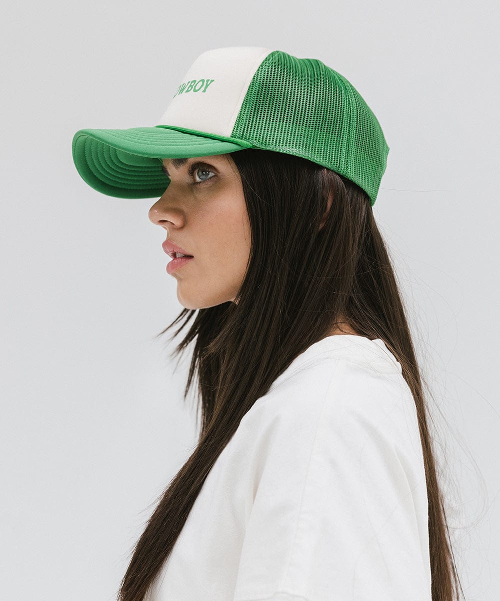 Woman wearing a cream and vintage green cap and a white t-shirt, facing sideways against a plain background #color_cream-vintage green