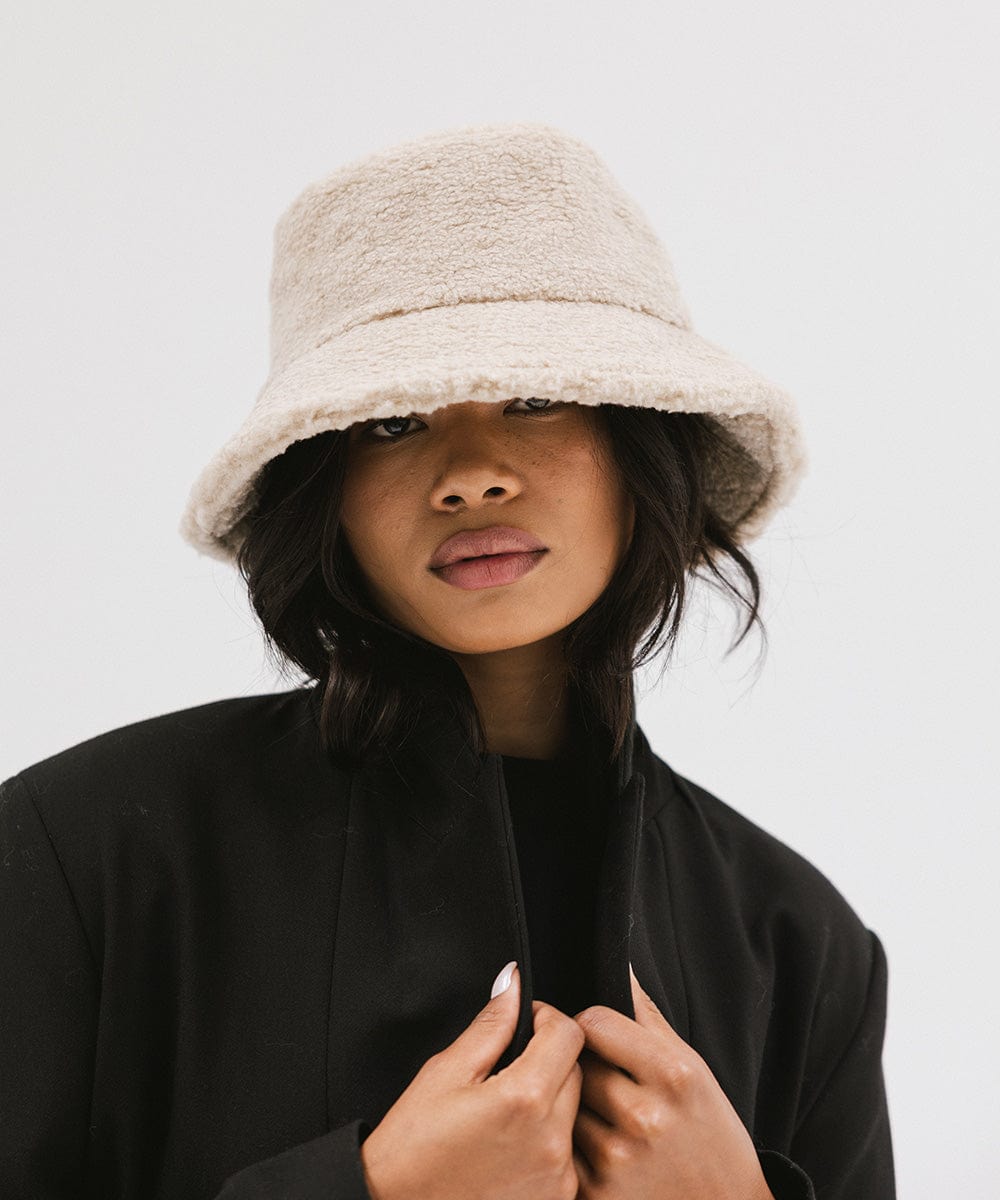 Woman wearing a cream sherpa bucket hat and a black coat against a plain background #color_cream