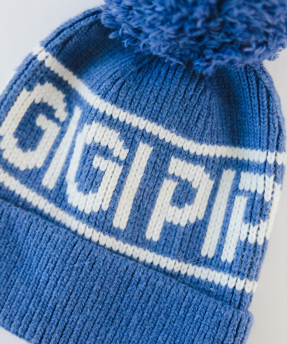 A close up image of an arctic blue colored knit beanie with pom-pom and 'GIGI PIP' branding on a white background #color_arctic blue