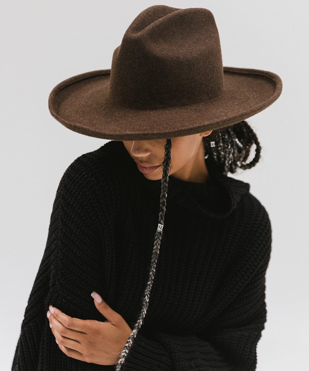 Woman wearing a mix brown colored western hat with a pencil brim and a tall crown, and a black sweater against a plain background #color_mix brown