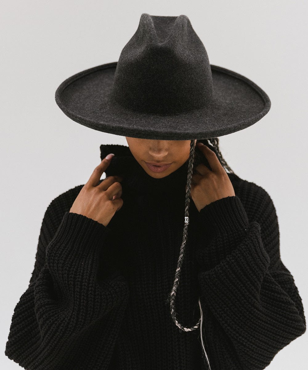 Person wearing a mix charcoal colored western hat with a pencil brim and a tall crown and a black sweater against a plain background #color_mix charcoal