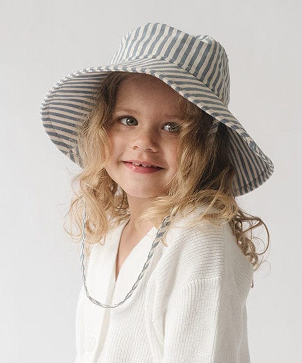 Young girl wearing a blue and white striped bucket hat and a white shirt against a plain background #color_striped-blue