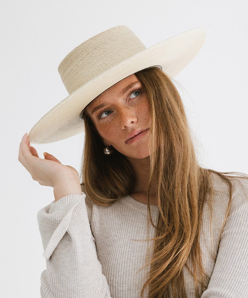 Woman wearing a natural colored straw boater hat and a white top against a plain background  #color_natural