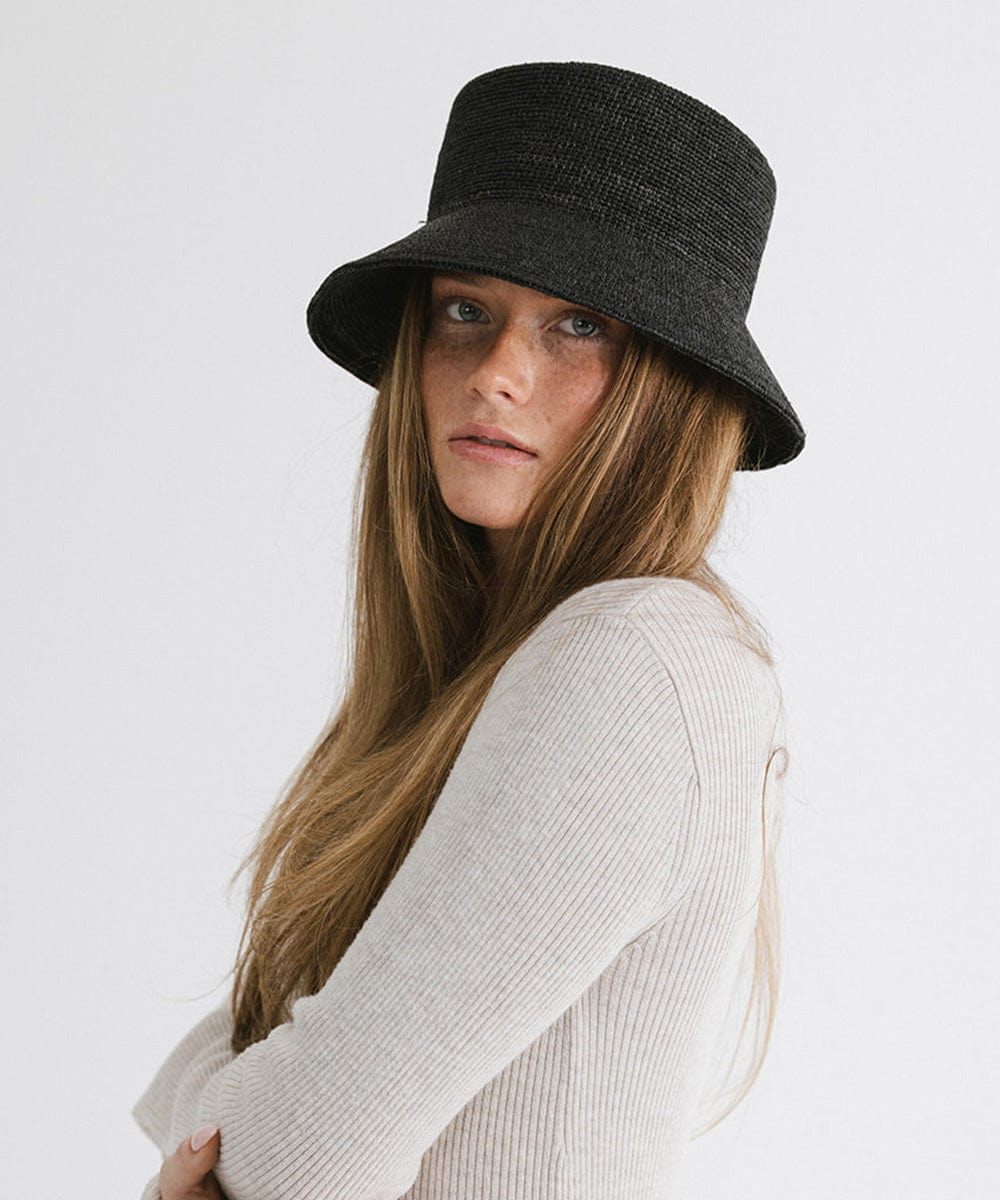Woman wearing a black packable bucket hat and a white top against a plain background #color_black