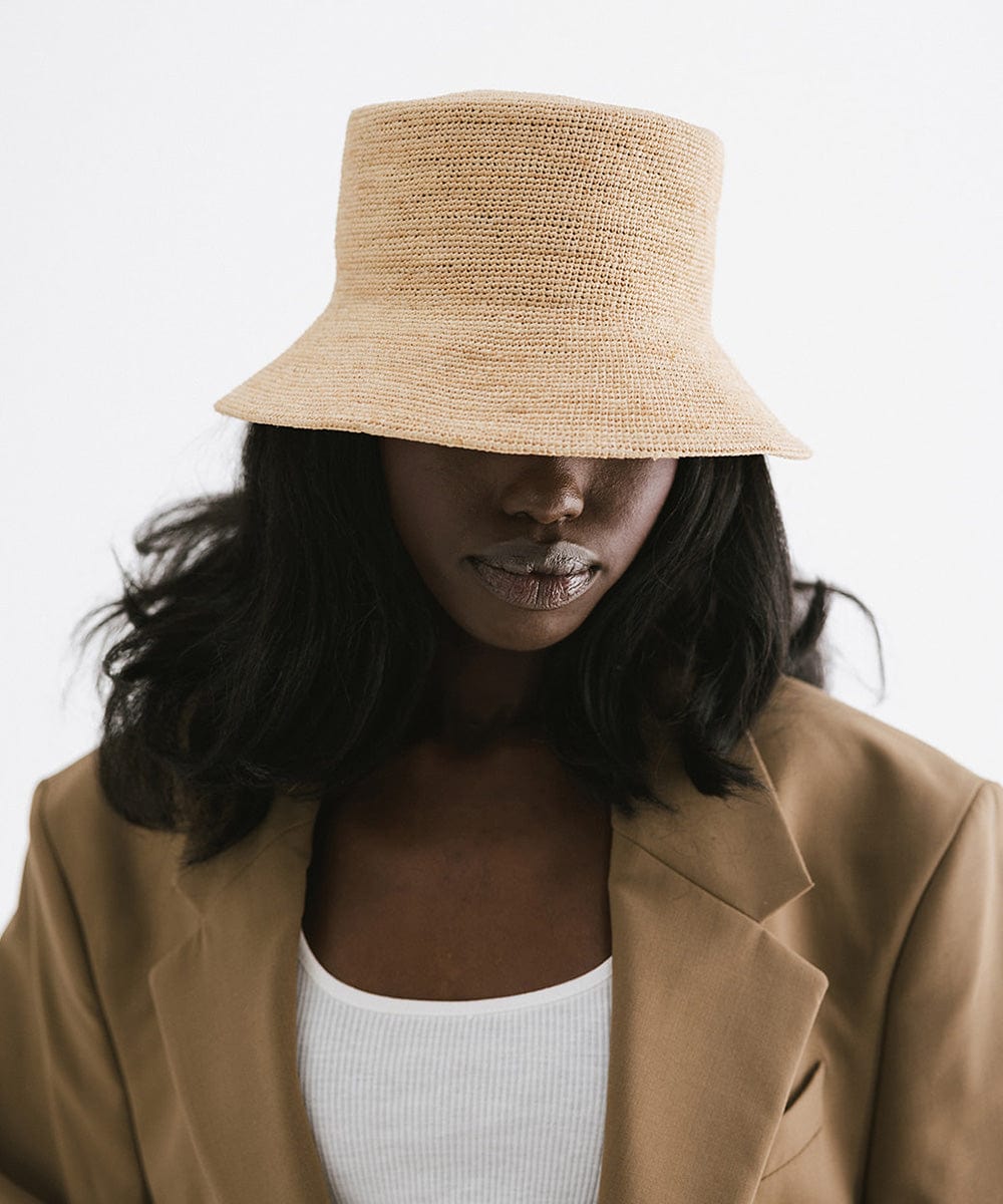 Woman wearing a natural colored packable bucket hat and a white top with a brown blazer against a plain background #color_natural