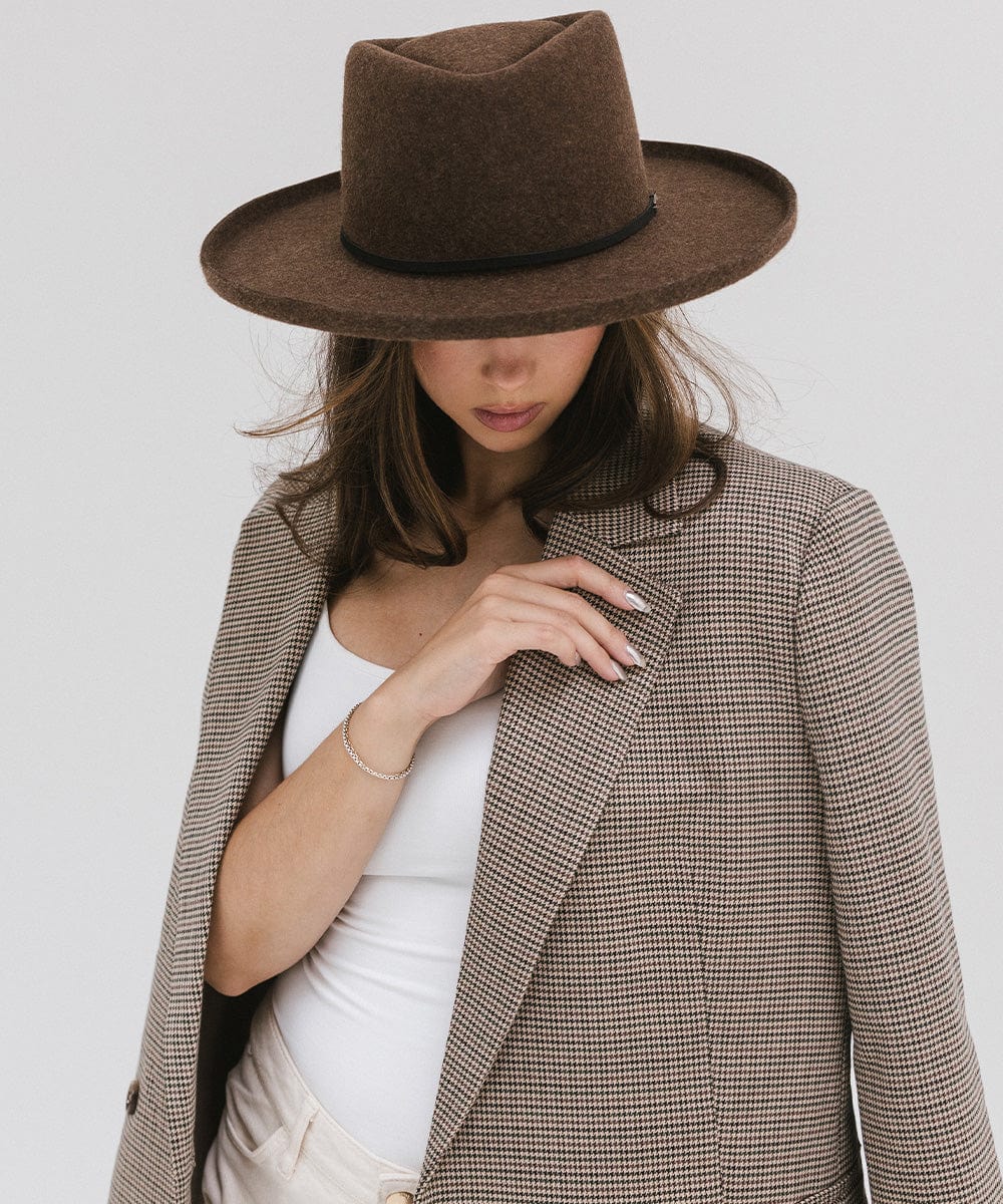 Woman wearing a mix brown Lennon pencil brim fedora hat with a hat band and a white top with a coat, posing against a plain background #color_mix brown