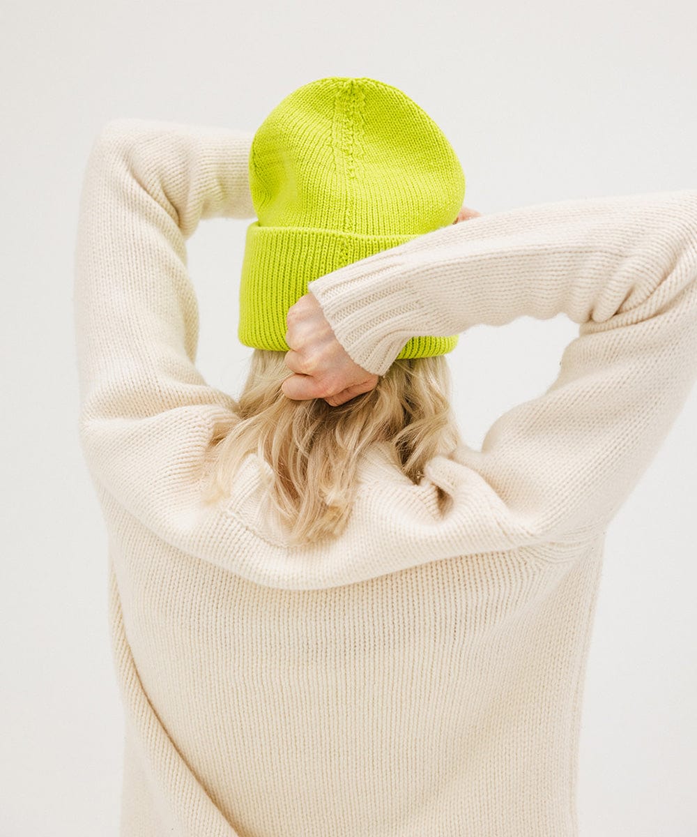 Person wearing a lime colored oversized knit beanie and a white sweater against a plain background #color_limeade