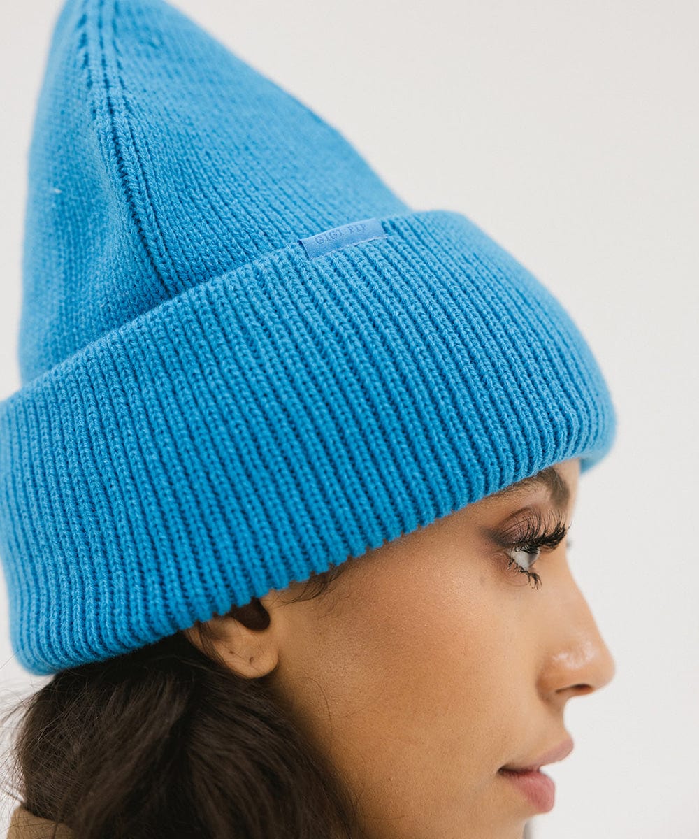 Woman wearing a blue oversized knit beanie, facing sideways against a plain background #color_deja blue
