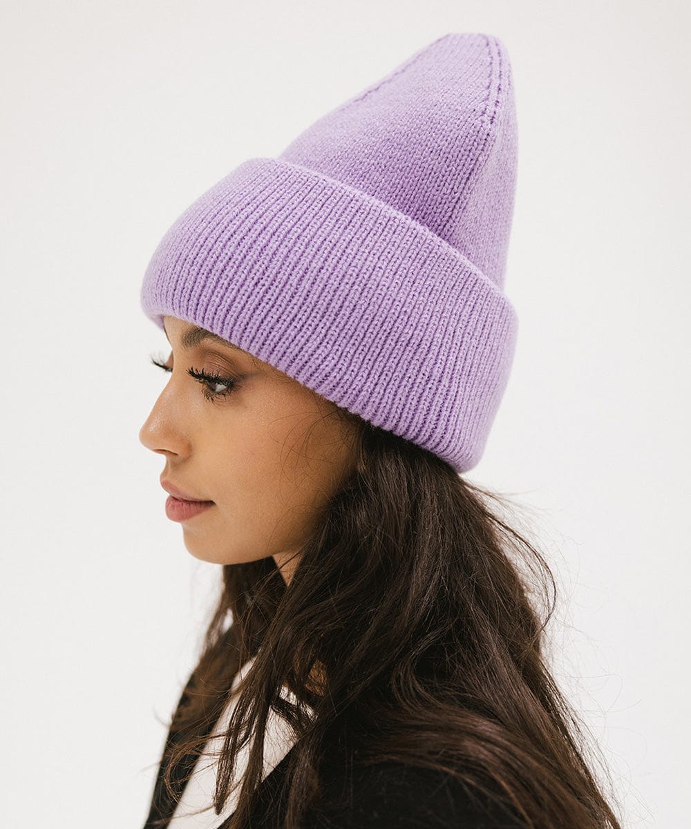 Woman wearing a lavender colored oversized knit beanie, facing sideways against a plain background #color_lavender
