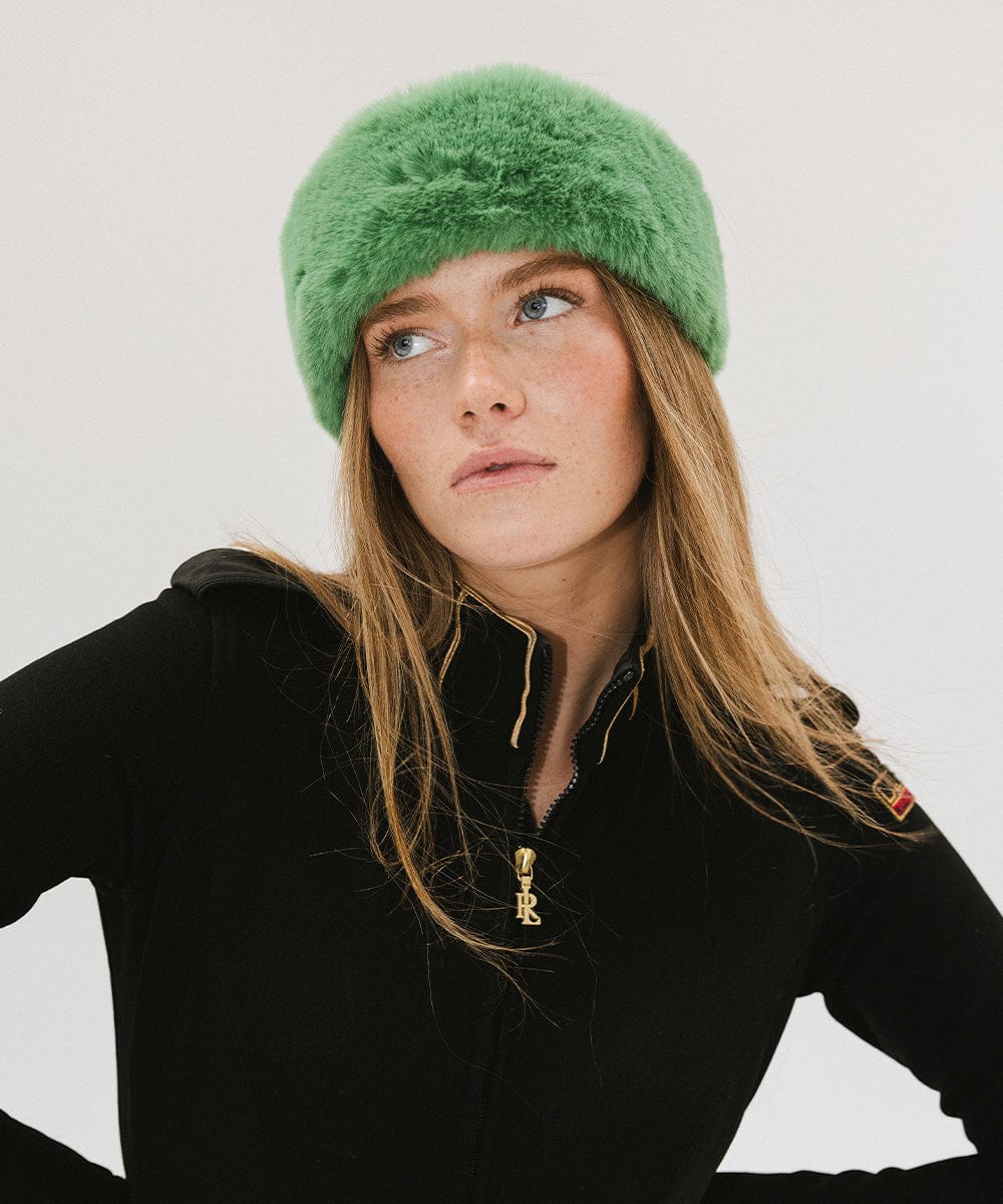 Woman wearing an evergreen colored fur headband and a black jacket against a plain background #color_evergreen