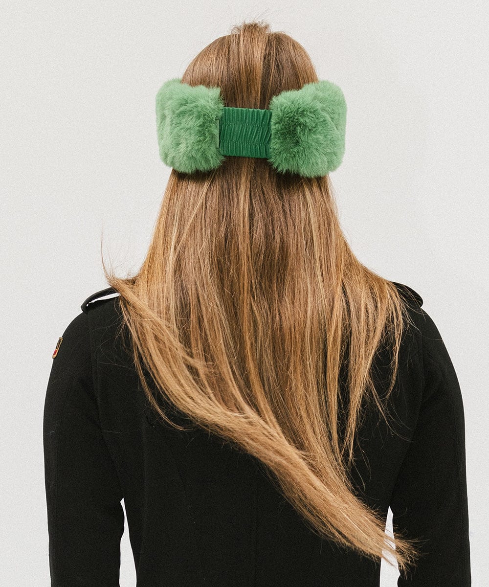 Woman with long hair wearing an evergreen colored fur headband and a black jacket, facing behind against a plain background #color_evergreen