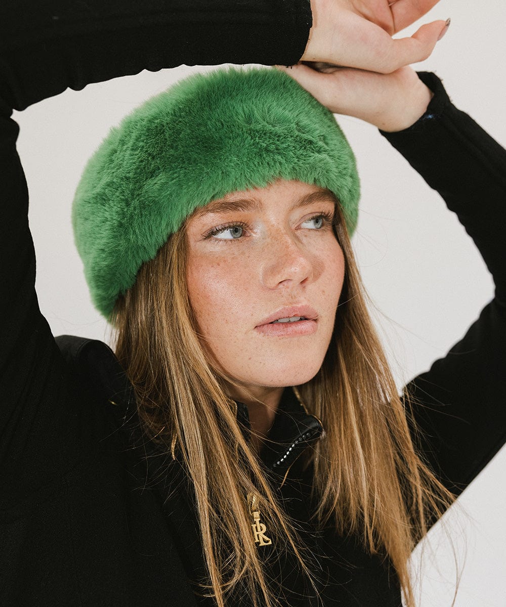 Woman wearing an evergreen colored fur headband and a black jacket, posing against a plain background #color_evergreen