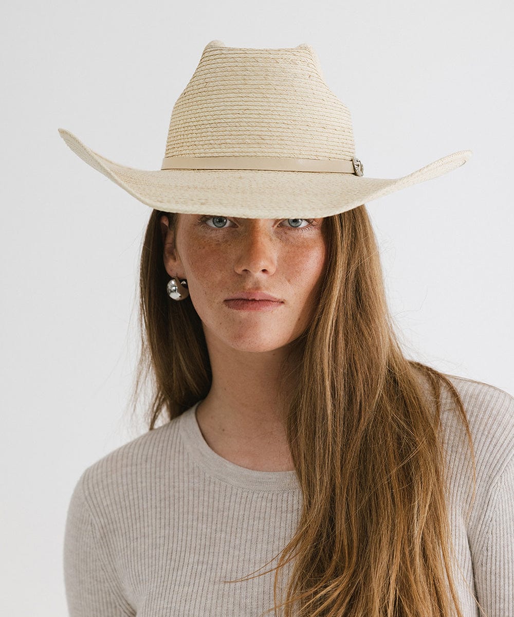 Woman wearing a natural colored straw cowgirl hat with an adjustable band and a grey t-shirt against a plain background #color_natural