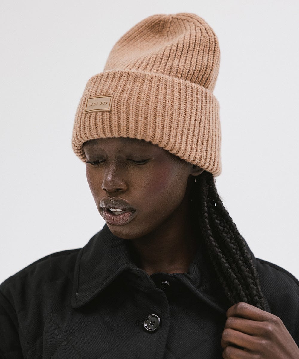 A woman wearing a brown colored ribbed beanie against a plain background #color_brown