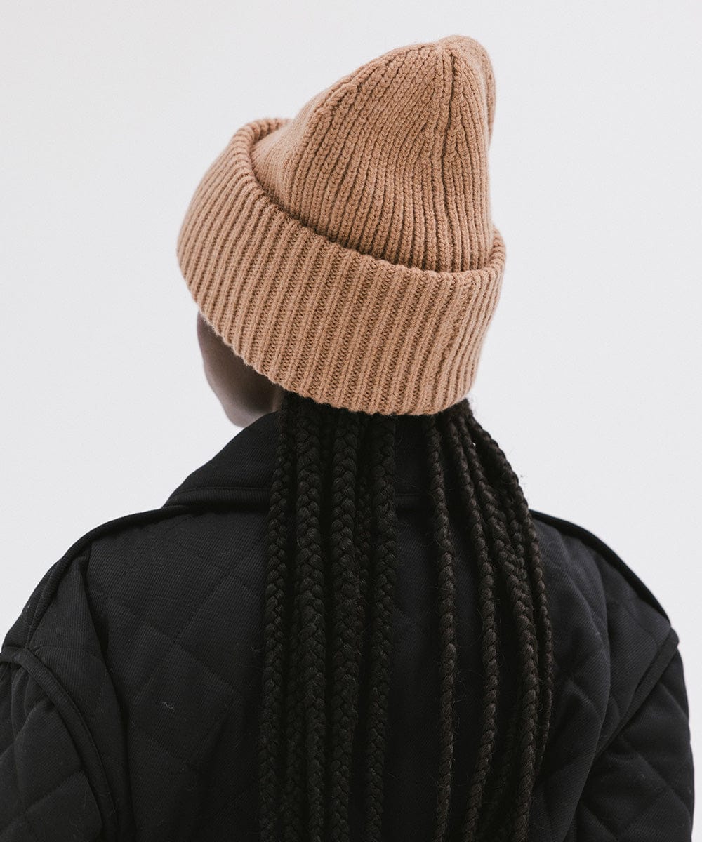 A person wearing a brown colored ribbed beanie and a black jacket, facing behind against a plain background #color_brown