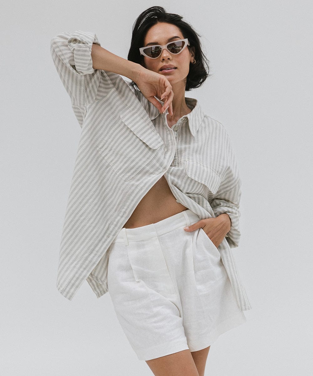 Woman wearing a light grey cat eye sunglasses, a white shirt with grey lines and white shorts against a plain background #color_light grey