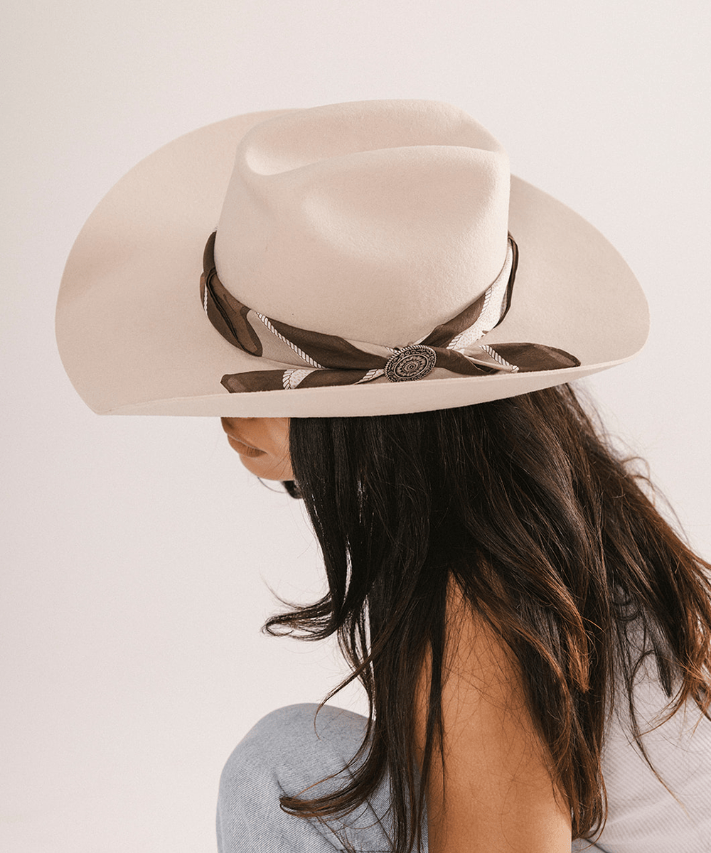 Woman wearing a beige cowboy hat with a chocolate colored bandana on a light background #color_chocolate