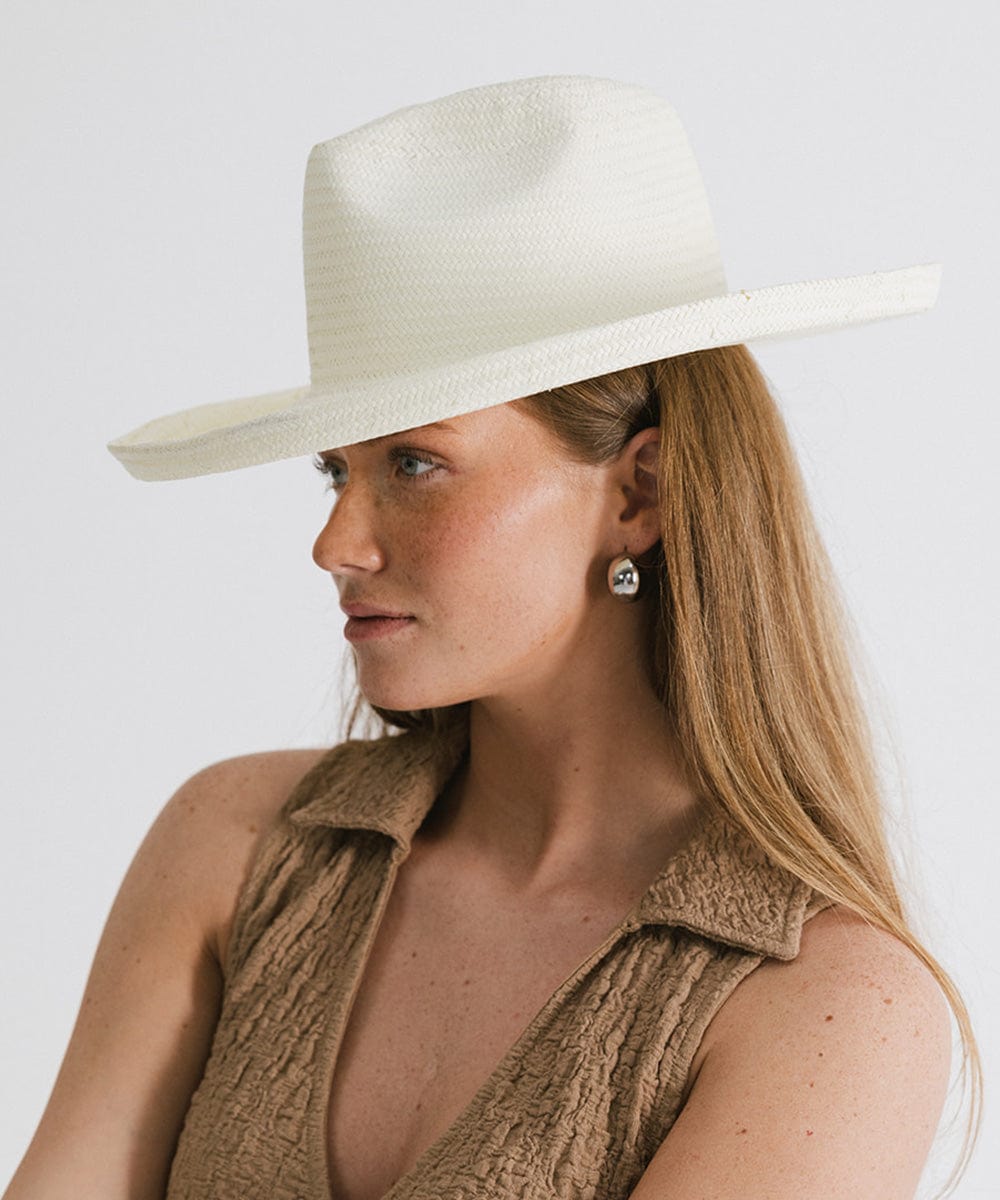 Woman wearing a white pencil brim fedora hat and a brown top, looking sideways against a plain background #color_white