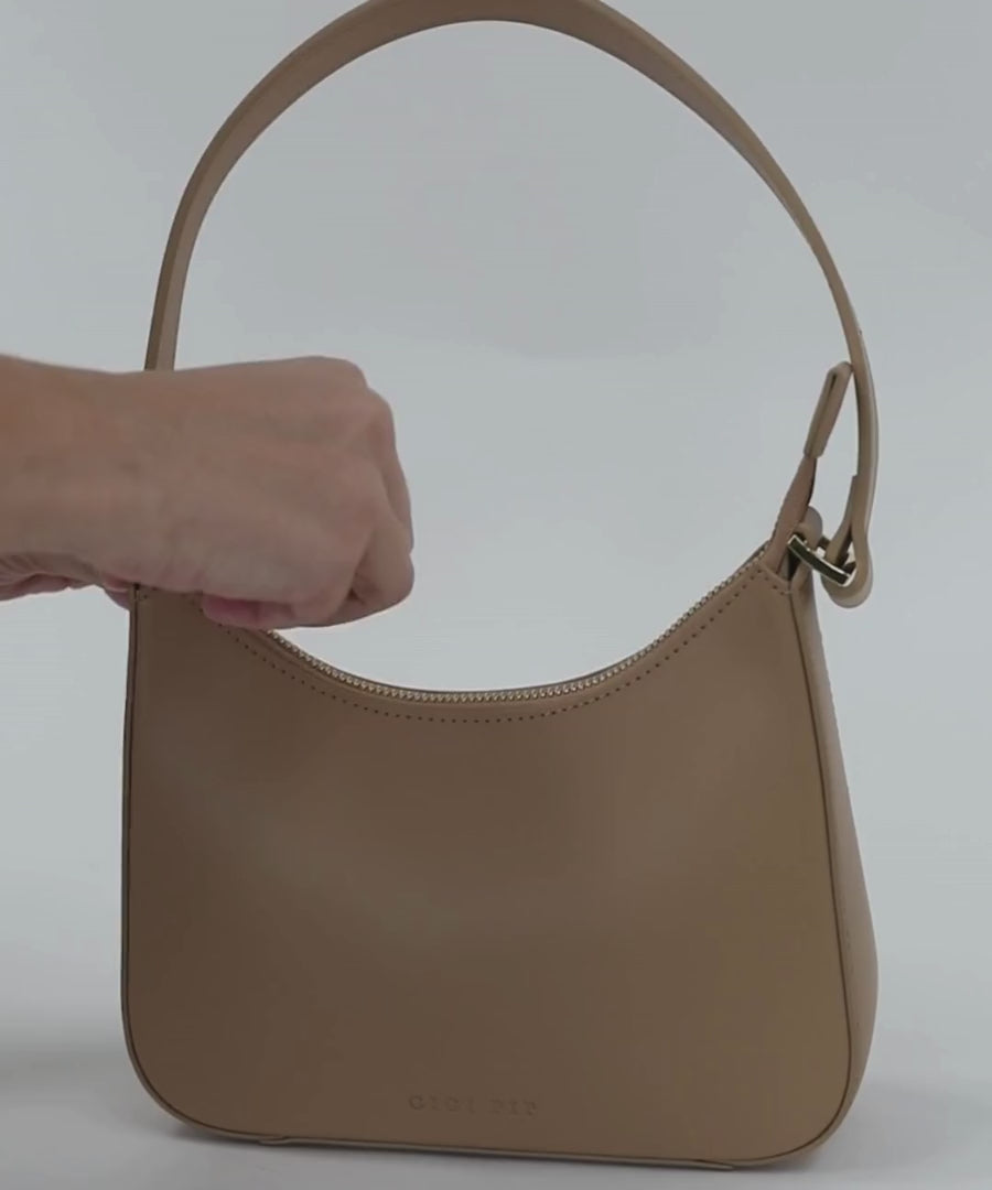 Person inserting various items into a tan genuine leather handbag on a plain background #color_tan