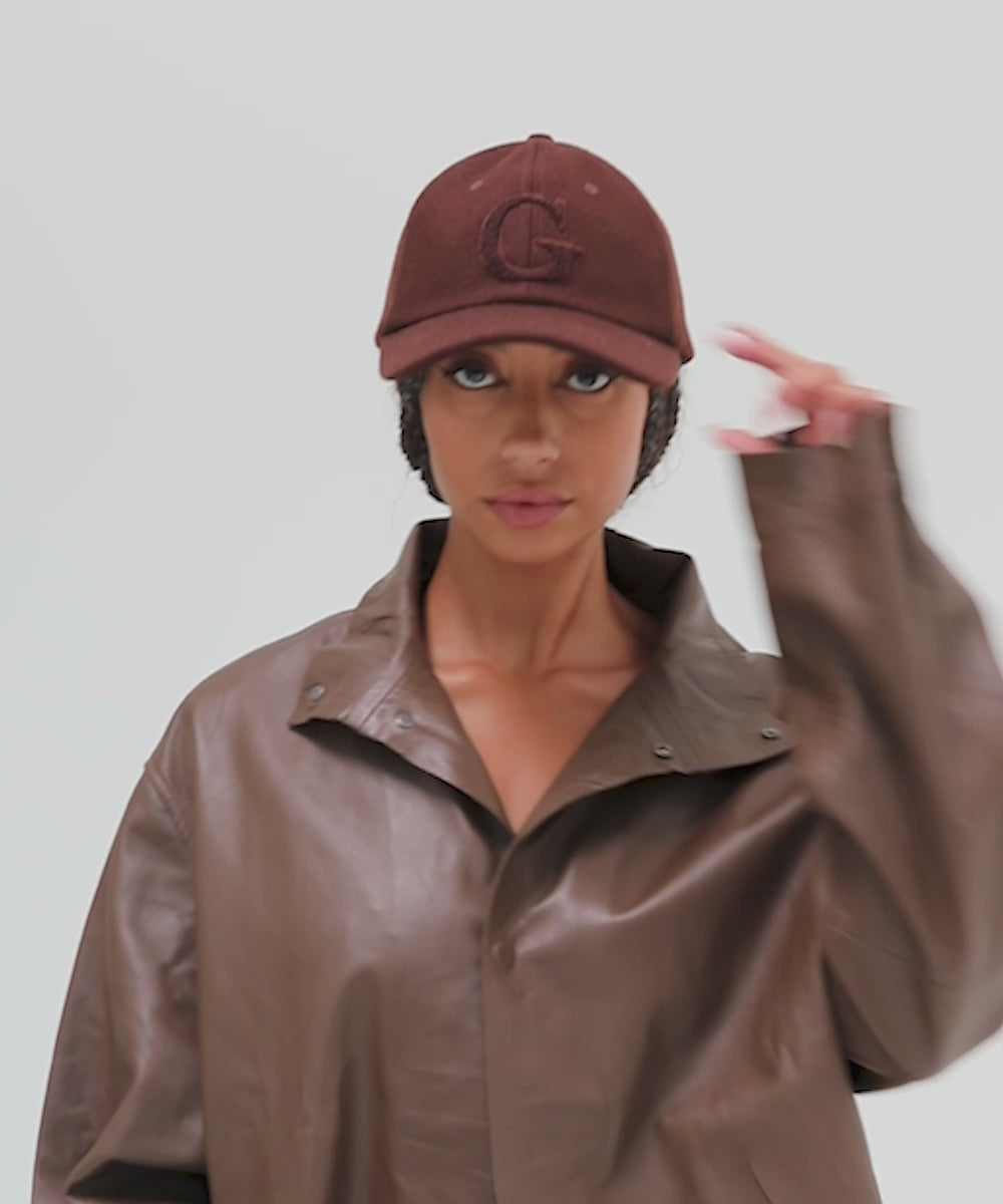 Woman wearing a chocolate brown baseball cap with the letter 'G' and a brown jacket, posing against a plain background #color_chocolate brown