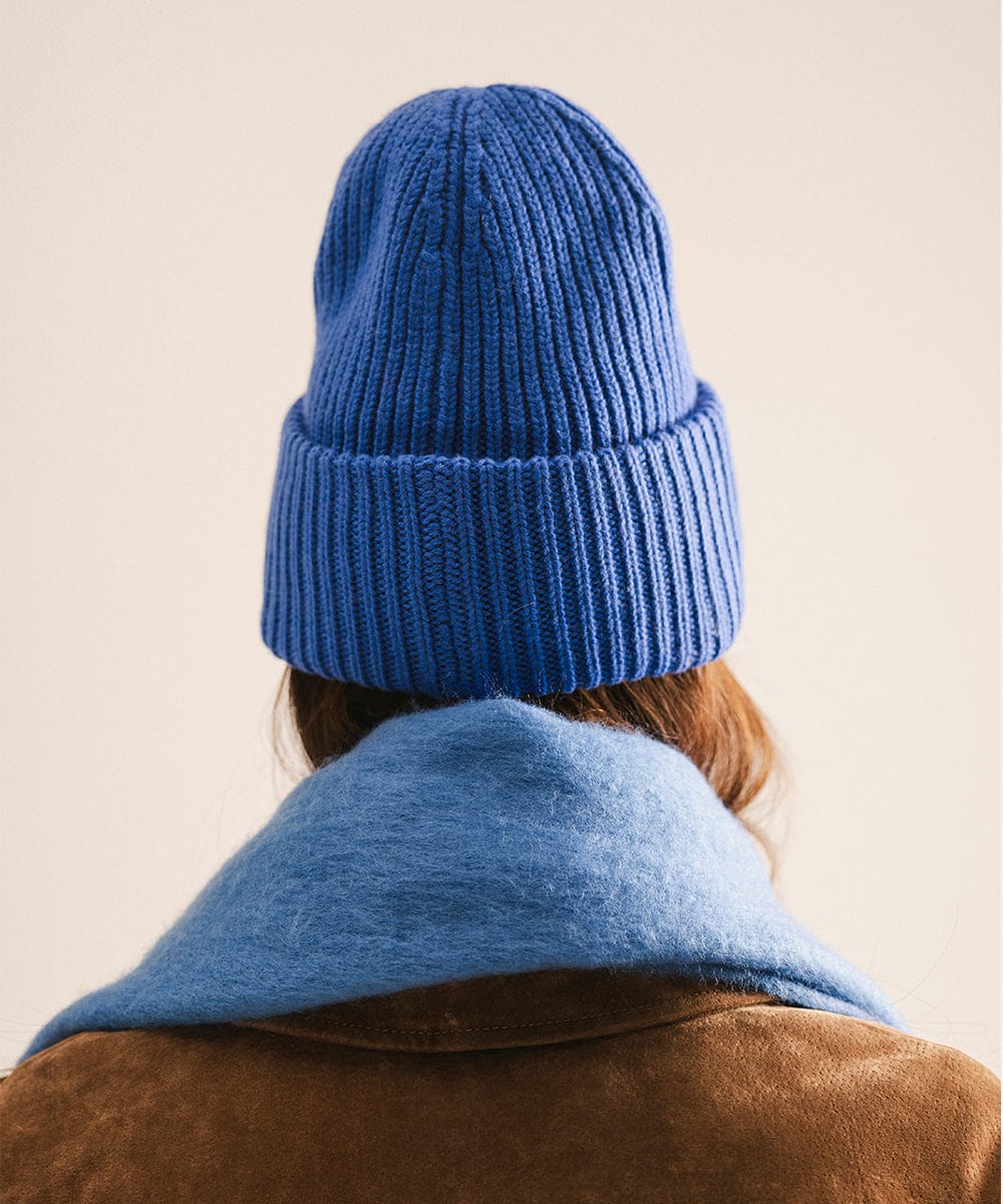 Person wearing a blue knit beanie and coat on a beige background #color_alpine blue