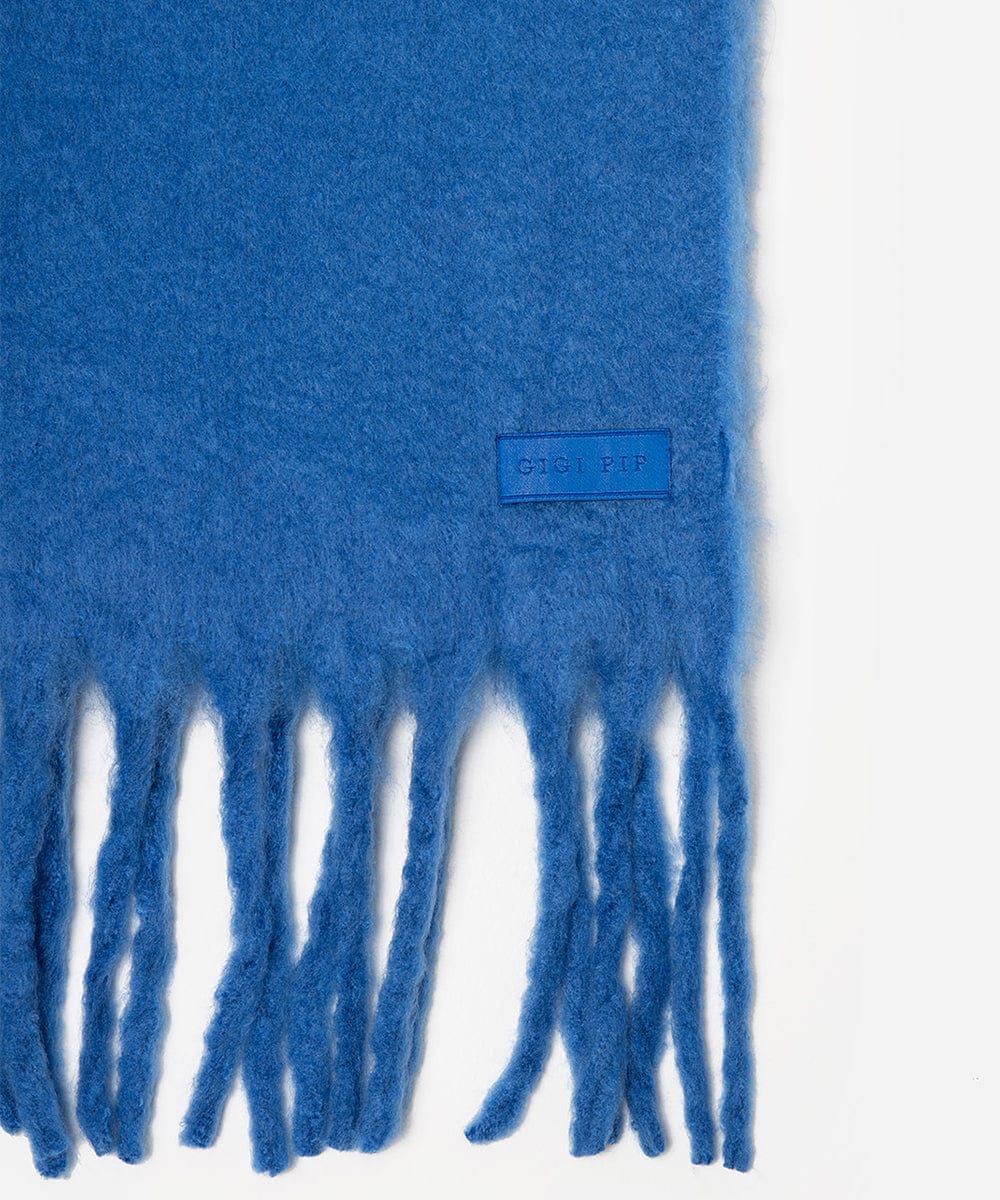 Blue scarf with fringes and a brand label on a white background #color_alpine blue