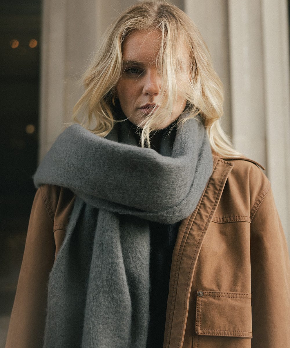 A person wearing a brown jacket and a grey oversized knit scarf, draped over the neck against a plain background #color_grey