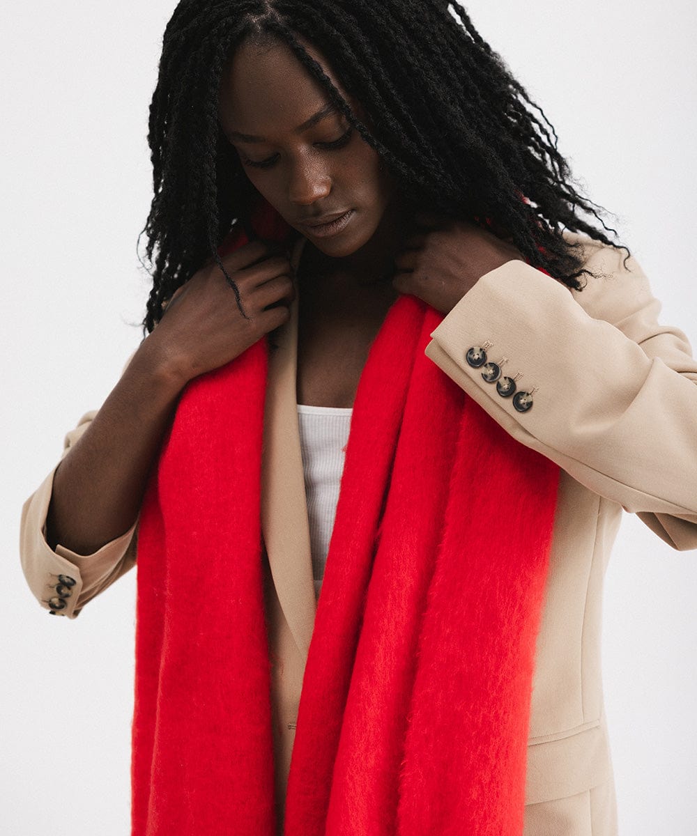 A person wearing a beige blazer, and a red oversized knit scarf, draped over the neck against a plain background #color_red